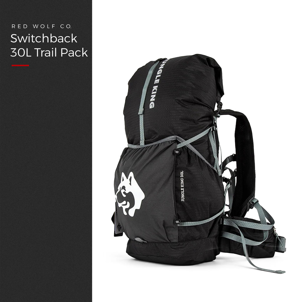 Blackout — Switchback 30L Trail Pack from the front three-quarter, roll-top closed, grey compression straps and padded hip belt, under a Red Wolf Co. title panel