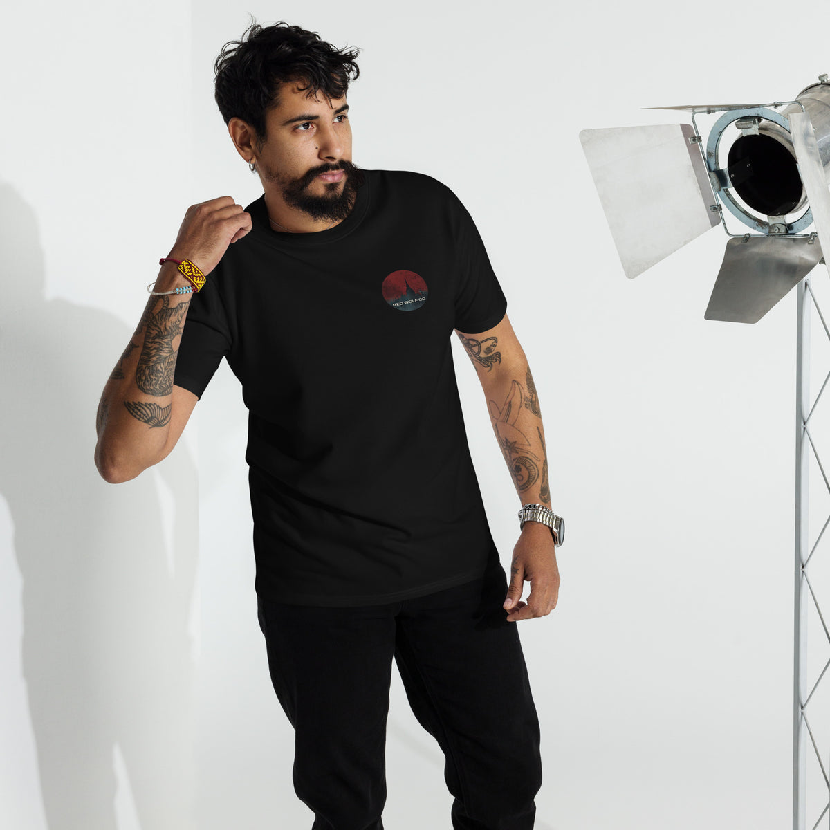 A man wearing the black Solace Tee, standing in a studio beside a light, with the circular Red Wolf Co wolf-and-red-moon badge on the left chest