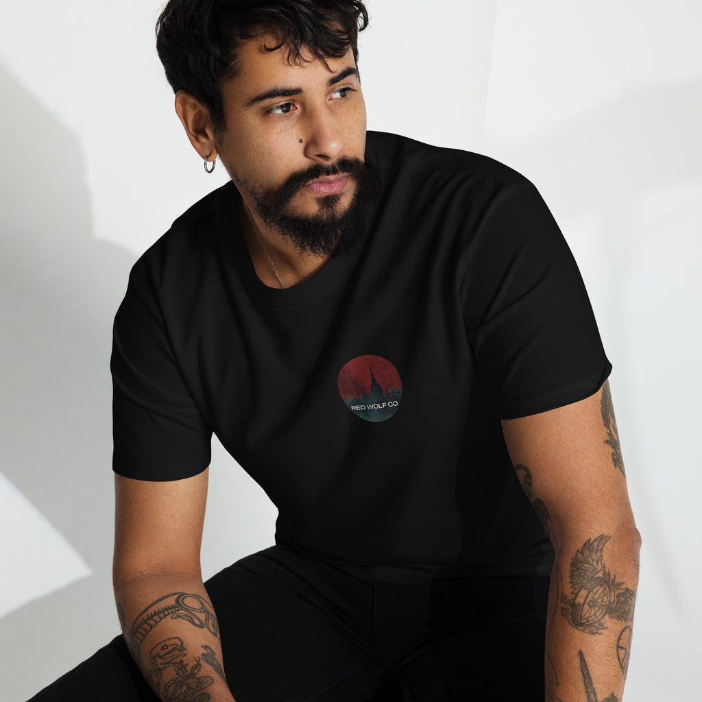 A man wearing the black Solace Tee, seated, with the circular Red Wolf Co wolf-and-red-moon badge on the left chest